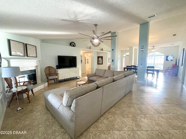 living area featuring a ceiling fan, a textured ceiling, light tile patterned floors, vaulted ceiling, and a tile fireplace