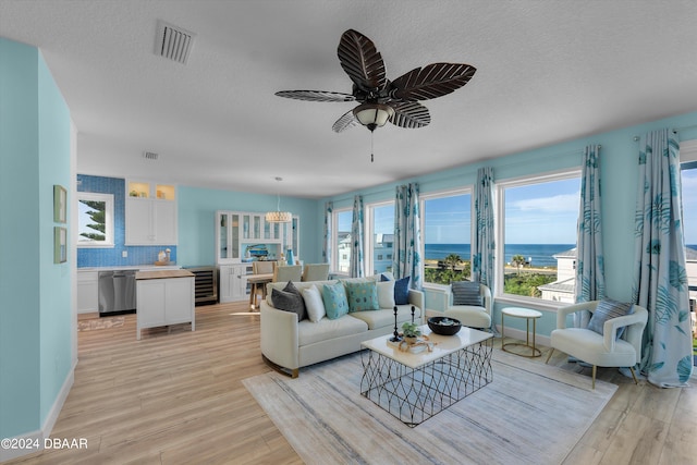 living room with light wood-type flooring, a water view, a textured ceiling, and ceiling fan