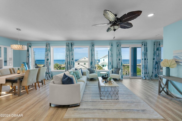 living room featuring light wood-type flooring, ceiling fan with notable chandelier, a water view, and a textured ceiling