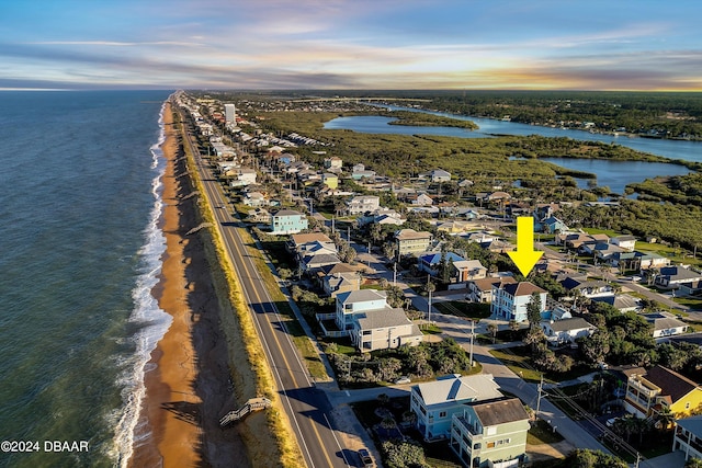 aerial view at dusk featuring a water view and a view of the beach