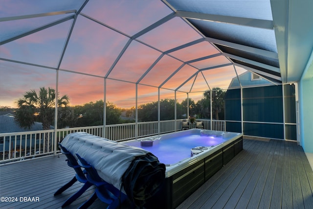 deck at dusk featuring an outdoor hot tub and a lanai