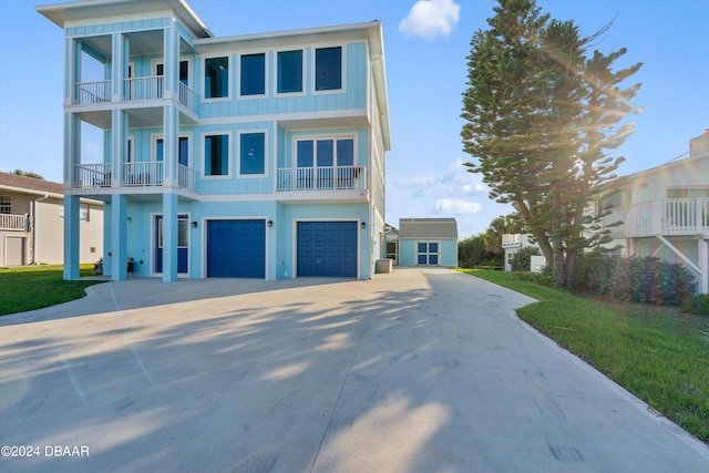 raised beach house featuring a garage, a front lawn, and a balcony