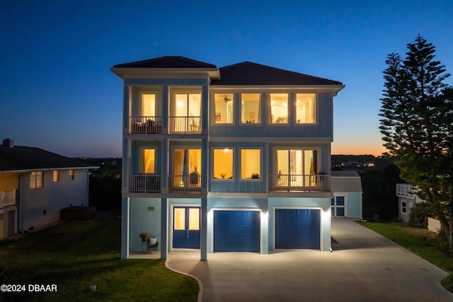 back house at dusk featuring a balcony, a garage, and a lawn