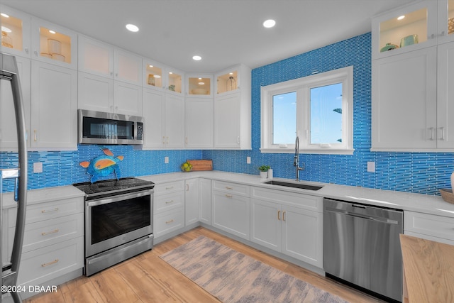 kitchen featuring light hardwood / wood-style flooring, sink, backsplash, white cabinetry, and appliances with stainless steel finishes