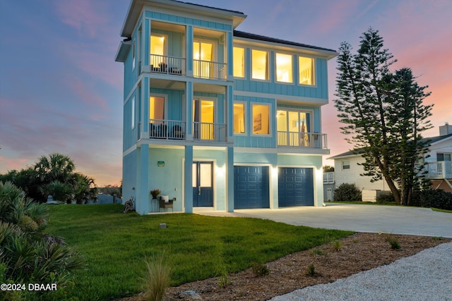 back house at dusk featuring a balcony, a garage, and a lawn