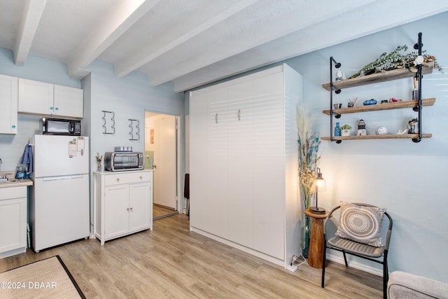 kitchen with white cabinets, beamed ceiling, white fridge, and light hardwood / wood-style flooring