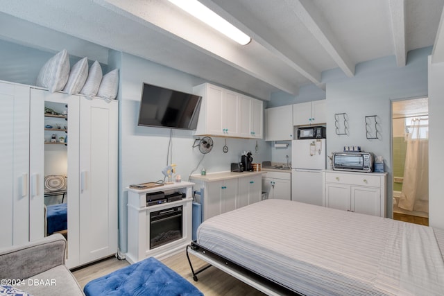 bedroom featuring white refrigerator, sink, light hardwood / wood-style floors, and beam ceiling