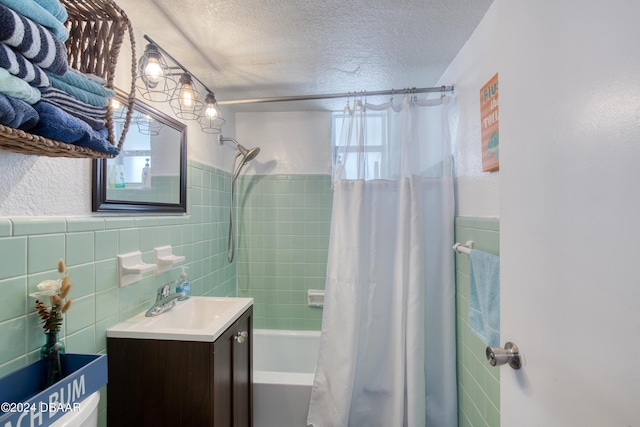 bathroom featuring a textured ceiling, vanity, shower / bath combination with curtain, and tile walls