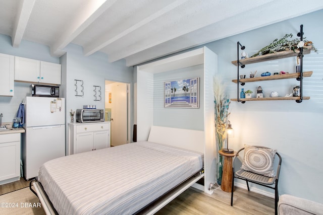 bedroom with white fridge, sink, beam ceiling, and light hardwood / wood-style flooring