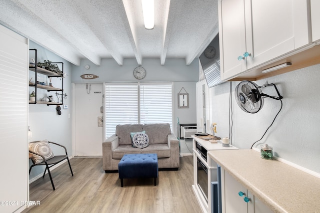 living room with a wall mounted air conditioner, beam ceiling, a textured ceiling, and light hardwood / wood-style flooring