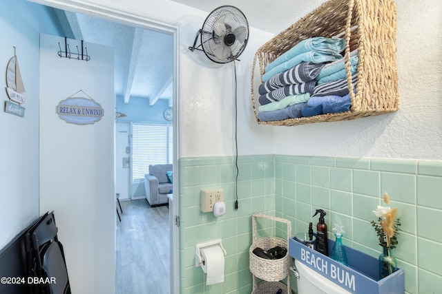 bathroom with beamed ceiling, wood-type flooring, a textured ceiling, and tile walls