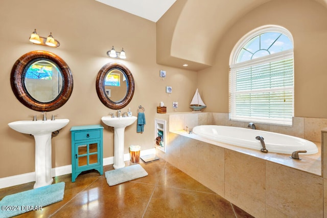 bathroom featuring tile patterned floors, dual sinks, a relaxing tiled tub, and lofted ceiling