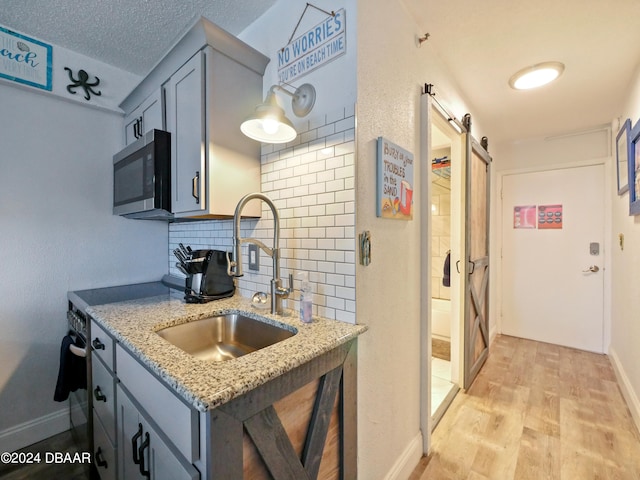 kitchen featuring light stone countertops, stainless steel appliances, a barn door, light hardwood / wood-style floors, and decorative backsplash