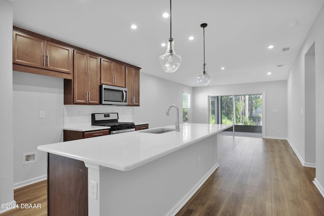 kitchen with decorative light fixtures, sink, stainless steel appliances, and a center island with sink