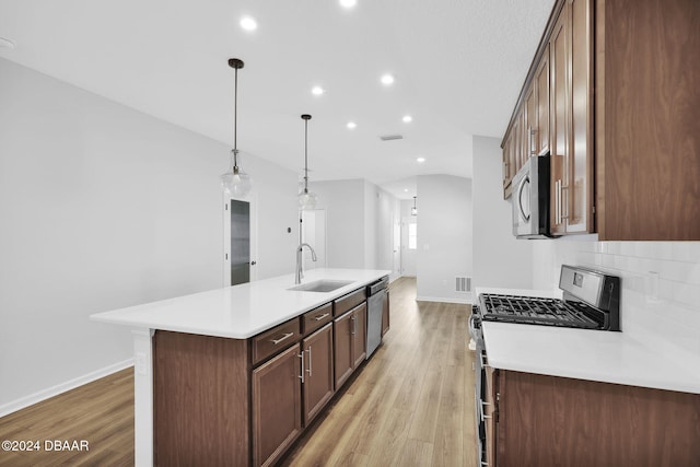 kitchen featuring sink, hanging light fixtures, a center island with sink, appliances with stainless steel finishes, and light wood-type flooring