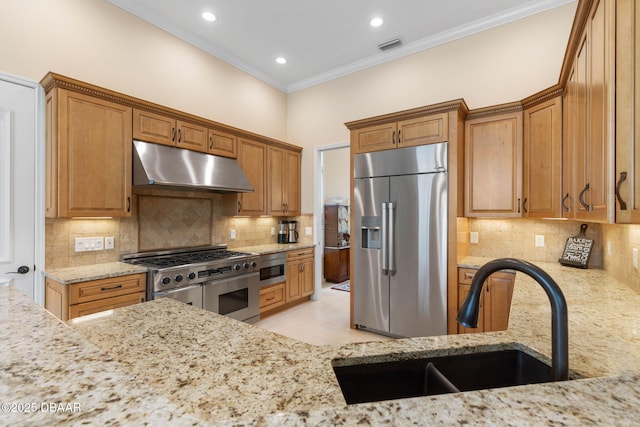 kitchen with a sink, ornamental molding, appliances with stainless steel finishes, under cabinet range hood, and light stone counters