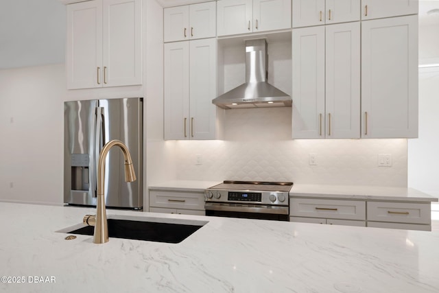 kitchen with wall chimney exhaust hood, sink, light stone counters, stainless steel appliances, and white cabinets