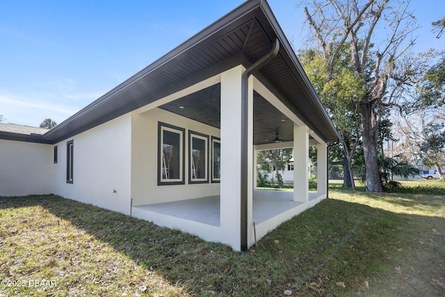 view of property exterior with ceiling fan, a patio, and a lawn