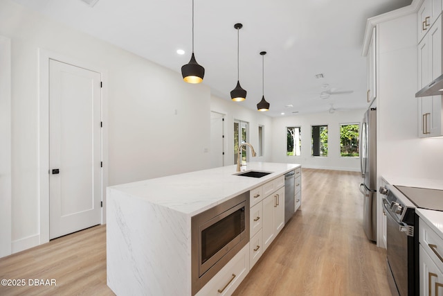 kitchen with decorative light fixtures, an island with sink, sink, white cabinets, and stainless steel appliances