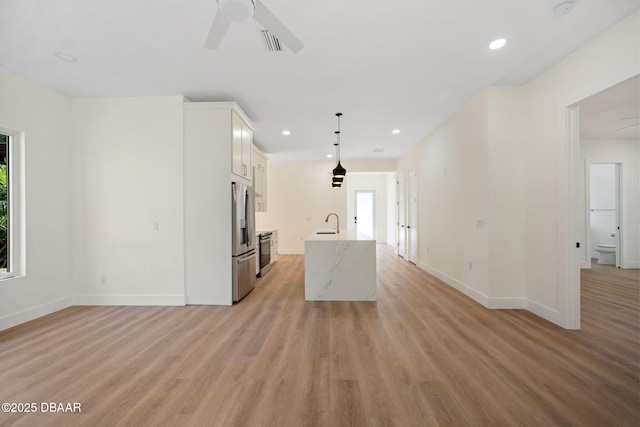 kitchen featuring white cabinetry, decorative light fixtures, stainless steel fridge, an island with sink, and ceiling fan