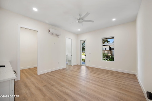 empty room featuring ceiling fan, a wall mounted AC, and light wood-type flooring