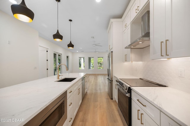 kitchen with wall chimney exhaust hood, sink, white cabinetry, light stone counters, and stainless steel appliances