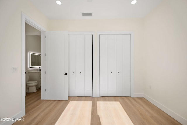 unfurnished bedroom with light hardwood / wood-style flooring and multiple closets