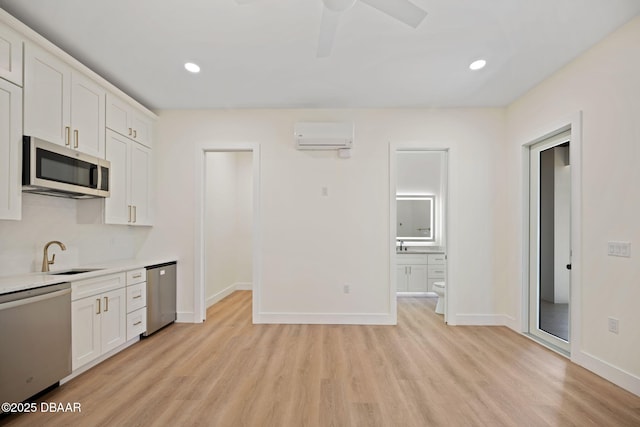 kitchen with appliances with stainless steel finishes, a wall mounted air conditioner, sink, white cabinets, and light hardwood / wood-style flooring