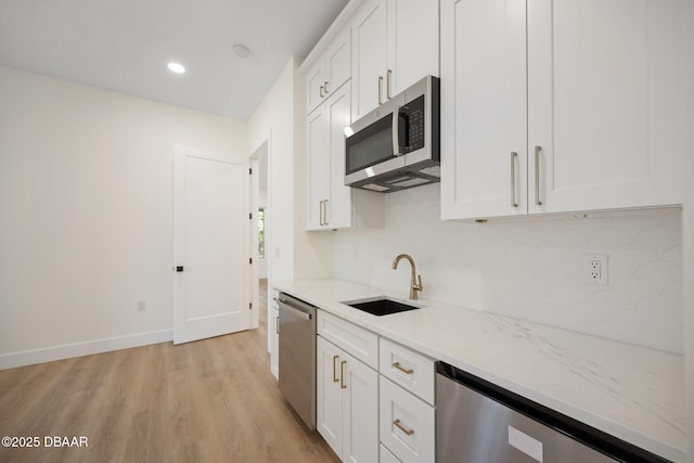 kitchen featuring appliances with stainless steel finishes, white cabinetry, sink, light stone countertops, and light wood-type flooring