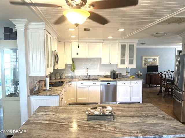 kitchen with appliances with stainless steel finishes, glass insert cabinets, white cabinetry, a sink, and dark stone countertops