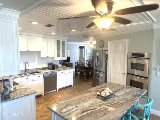 kitchen with stainless steel appliances, glass insert cabinets, white cabinetry, a sink, and dark stone counters