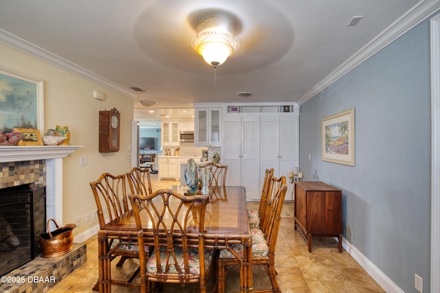 dining space featuring a fireplace with raised hearth, crown molding, visible vents, and baseboards