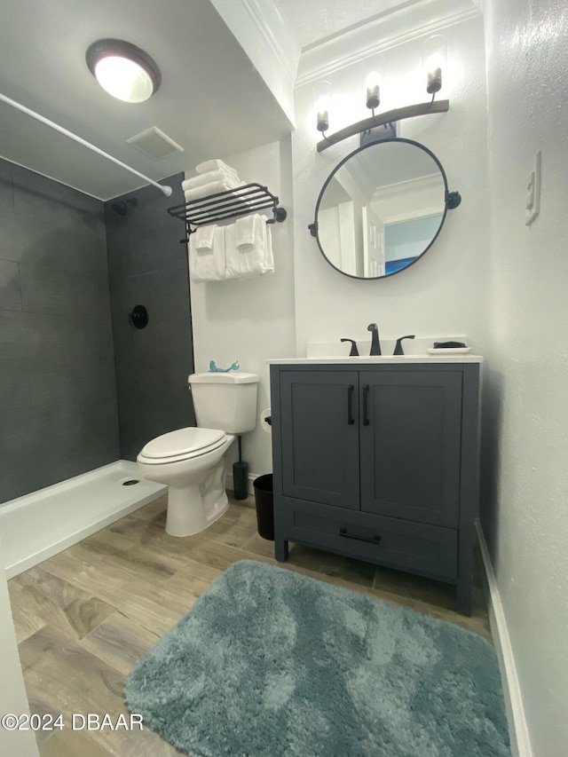 bathroom featuring wood-type flooring, toilet, a tile shower, ornamental molding, and vanity