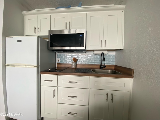 kitchen with white refrigerator, sink, ornamental molding, backsplash, and white cabinetry