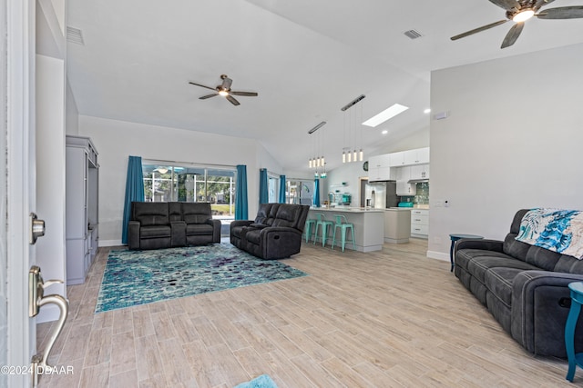 living room featuring a skylight, high vaulted ceiling, ceiling fan, and light hardwood / wood-style floors