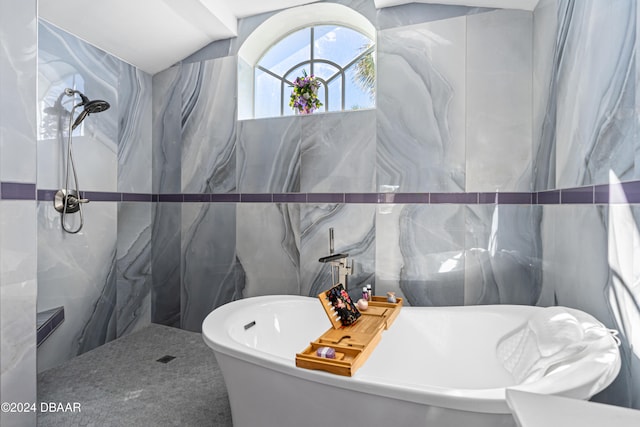 bathroom featuring lofted ceiling, a bath, and tile walls