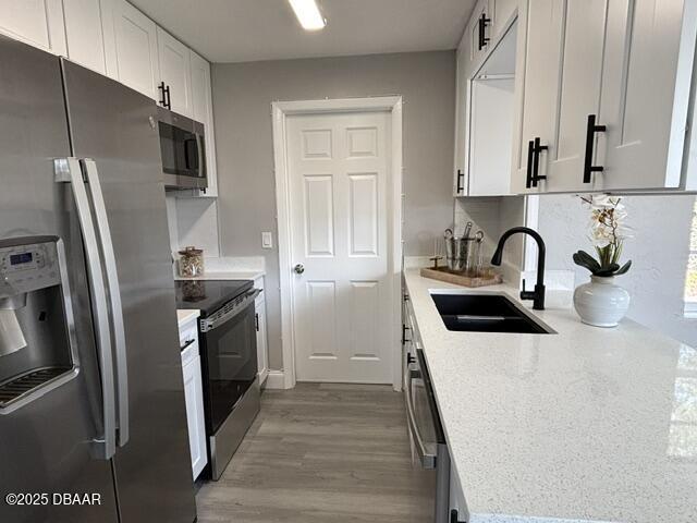 kitchen with sink, light hardwood / wood-style flooring, white cabinetry, stainless steel appliances, and light stone counters