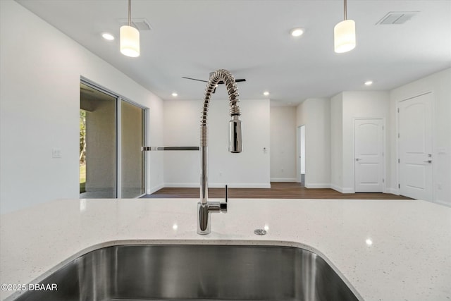 room details featuring light stone counters, hanging light fixtures, hardwood / wood-style flooring, and sink