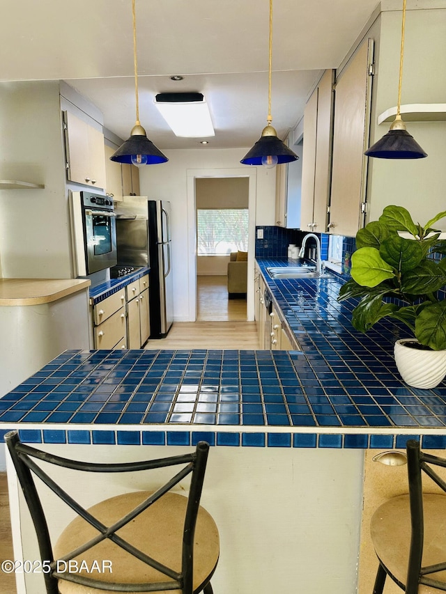 1011 S Peninsula Dr, Daytona Beach, FL 32118 - kitchen featuring stainless steel appliances, a sink, tile counters, light wood-style floors, and pendant lighting