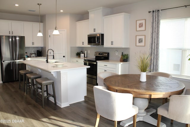 kitchen featuring sink, hanging light fixtures, appliances with stainless steel finishes, a kitchen island with sink, and white cabinets