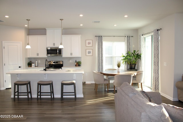 kitchen featuring appliances with stainless steel finishes, decorative light fixtures, sink, white cabinets, and a center island with sink