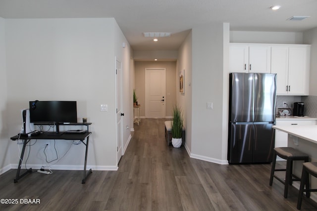 kitchen with dark wood-type flooring, stainless steel fridge, a breakfast bar area, tasteful backsplash, and white cabinets