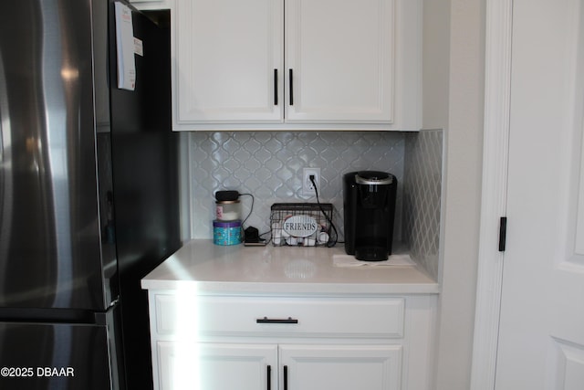 room details featuring decorative backsplash, white cabinets, and black fridge