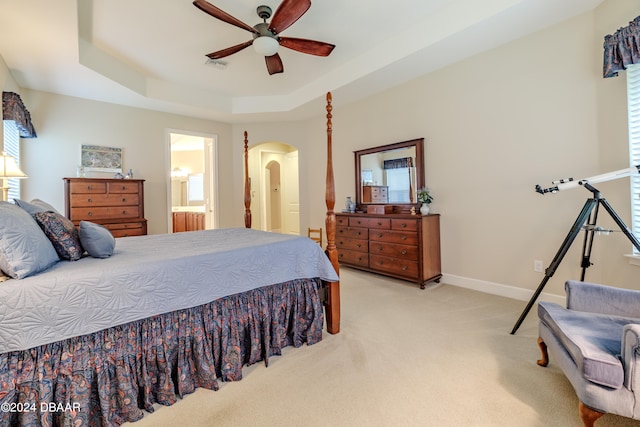 bedroom featuring ensuite bath, a raised ceiling, ceiling fan, and light colored carpet