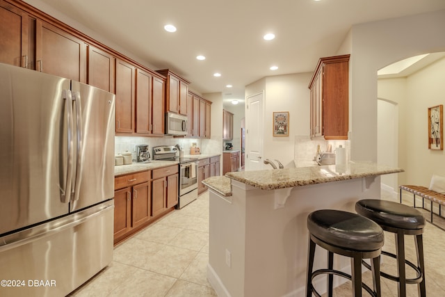 kitchen featuring stainless steel appliances, tasteful backsplash, light stone countertops, a kitchen bar, and light tile patterned floors