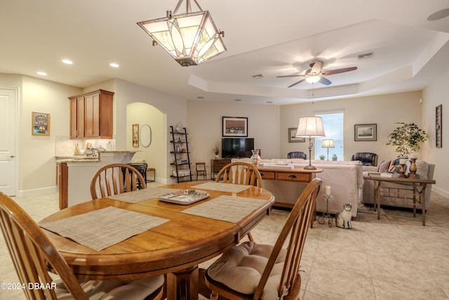 dining area featuring light tile patterned floors, ceiling fan, and a raised ceiling