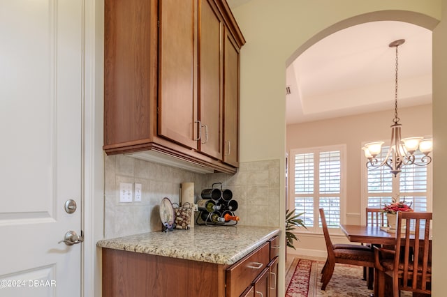 kitchen with light stone counters, decorative light fixtures, a tray ceiling, a chandelier, and decorative backsplash