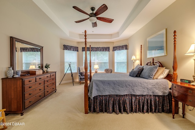 bedroom with ceiling fan, light carpet, and a tray ceiling