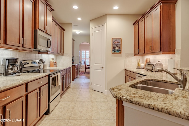 kitchen with sink, light stone counters, appliances with stainless steel finishes, light tile patterned floors, and backsplash