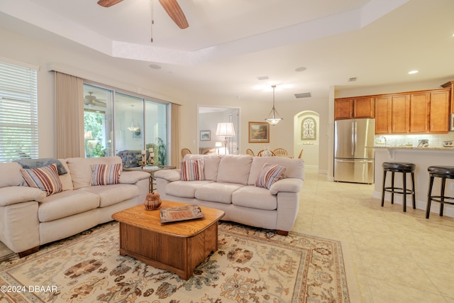 tiled living room featuring ceiling fan and a raised ceiling